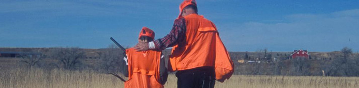two men in orange vests with backs to camera going hunting