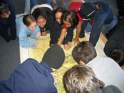 A group of children gather around a large topographical map.