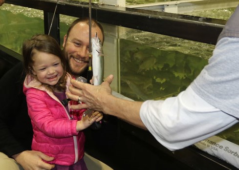 Young girl with Dad smailes as volunteer shows her fish she caught in CPW tank