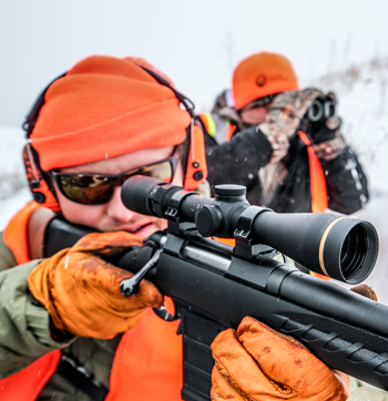 A man scouts with binoculars while another man looks through his rifle sight.