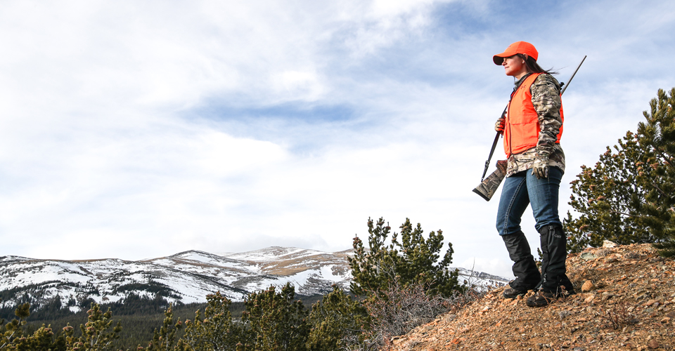 Woman in hunter orange and camo with rifle slung over shoulder