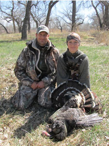 Man and youth pose with harvested tom turkey.