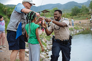 Park ranger assisting youth and volunteer to remove fish hook at education event