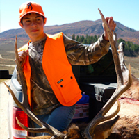 A youth in hunter orange poses with the bull elk he harvested.