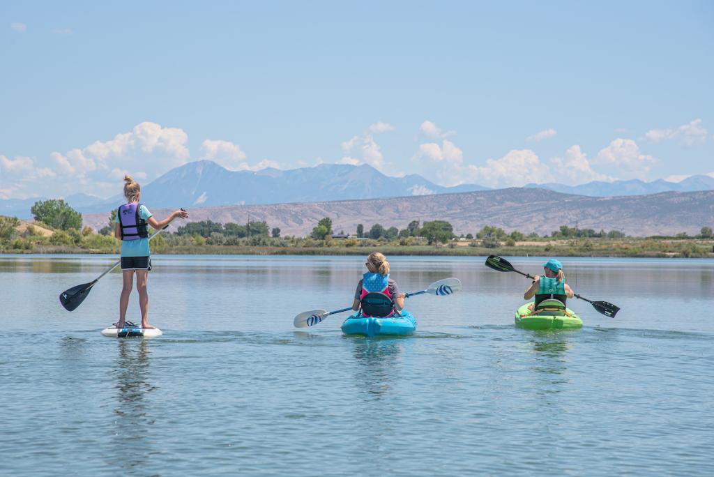 People recreating on a lake - two kayakers and one paddleboarder.