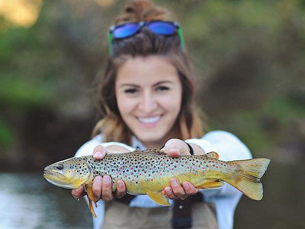 Female wearing sunglasses holds up fish to camera