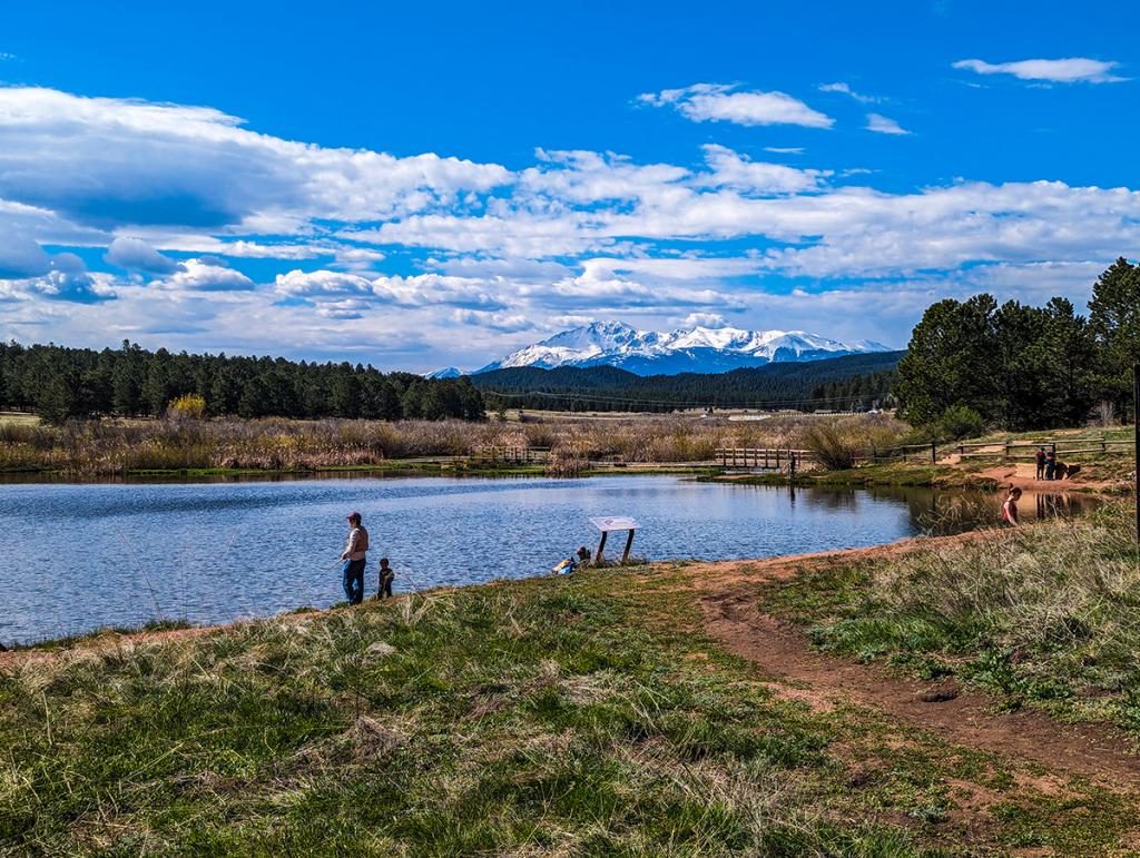 Man and child fish at Manitou lake. View of lake, blue sky and Pikes Peak in the distance