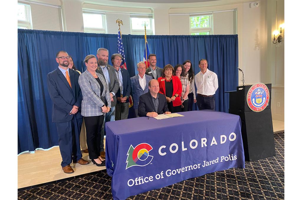 Governor Jared Polis sits at a table signing Senate Bill 25-168