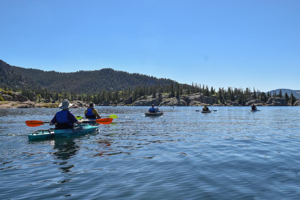 Five kayakers wearing lifejackets on water with trees in the background