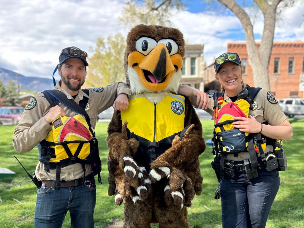 Two CPW park rangers wearing life vests and standing next to the CPW eagle mascot