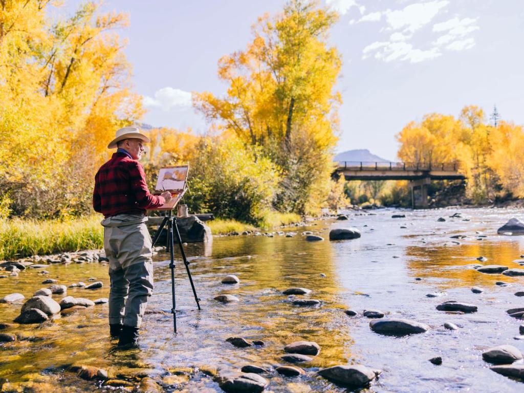 Male painter stands in creek to paint yellow trees