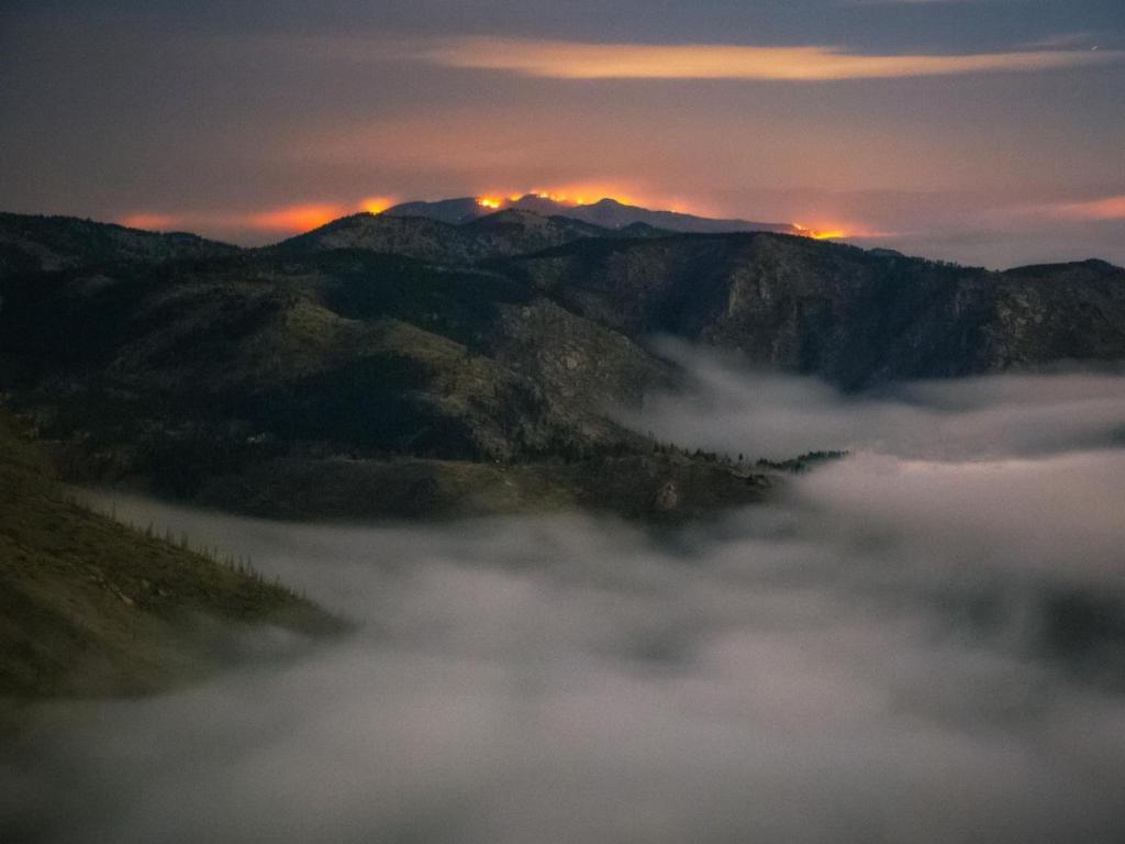 Wildfire smoke covers a mountain landscape with fire flames in the background
