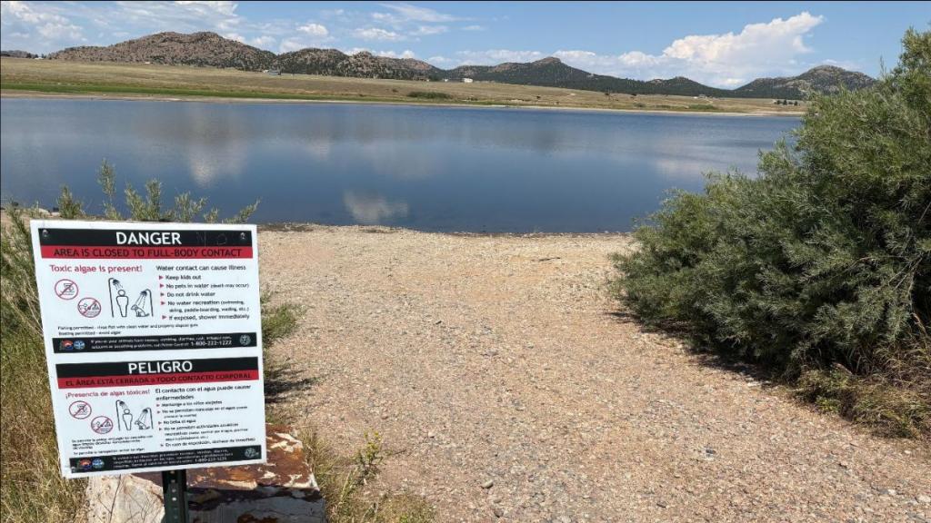 A sign near the water warns the public to avoid the toxic algae bloom in DeWeese Reservoir State Wildlife Area.