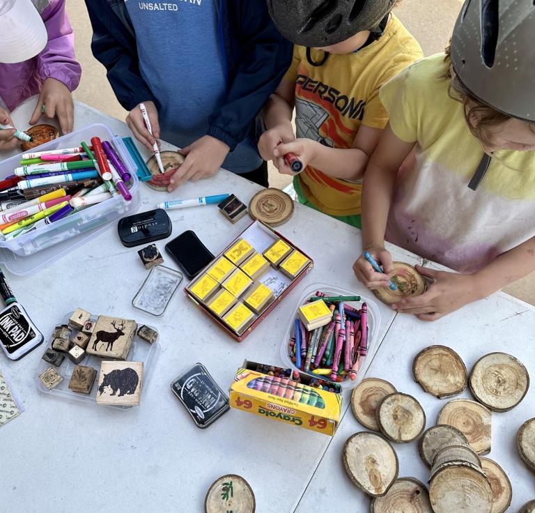 Children wearing bike helmets staring down at a table full of craft supplies.