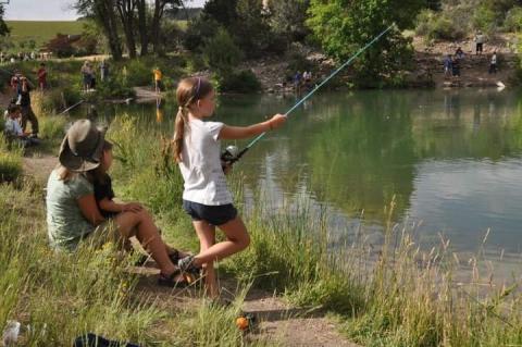 Young girl casting fishing pole while mom watches