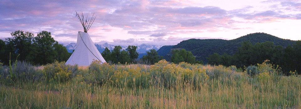 teepee in tall grass with mountains and sunset in background