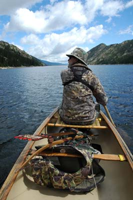 Bowhunter canoeing across lake.