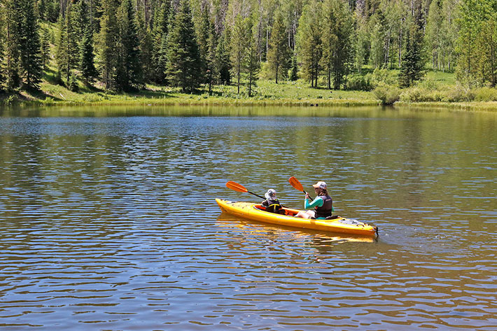 Mom and daughter kayaking on lake with trees and mountains in background