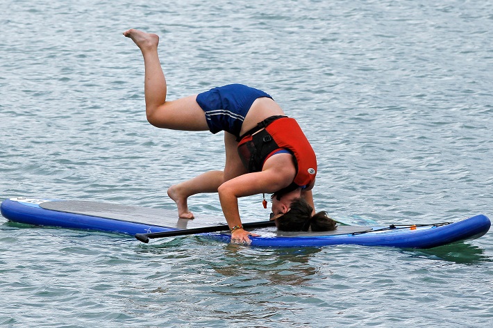 woman in life vest going into headstand on paddle board