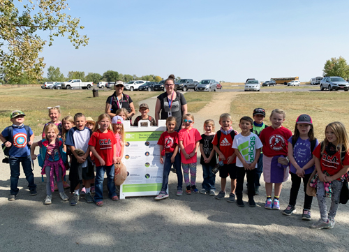 A group of school children and their chaperones pose next to a sign about the 7 leave no trace principles. 